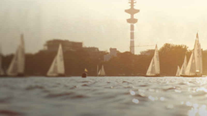 Segelboote auf der Binnenalster in Hamburg bei Sonnenuntergang, Fernsehturm im Hintergrund, ruhige Wasseroberfläche.