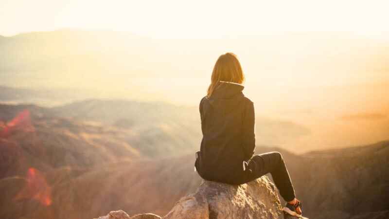 Frau sitzt auf dem Gipfel eines Berges und beobachtet den Sonnenaufgang