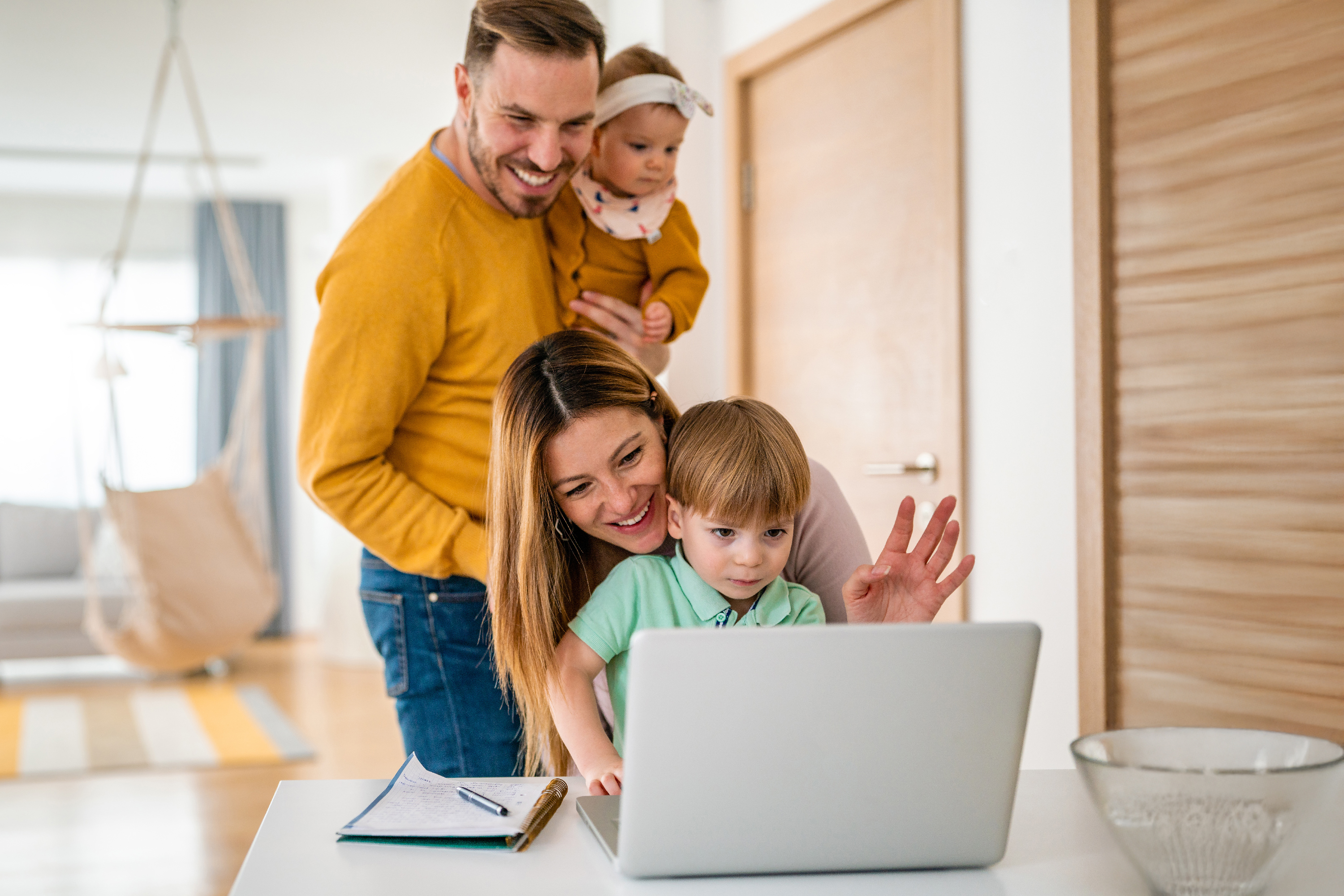 Familie im Wohnzimmer, Eltern und zwei Kinder lächeln gemeinsam am Laptop, fröhliche Kommunikation im modernen Zuhause.