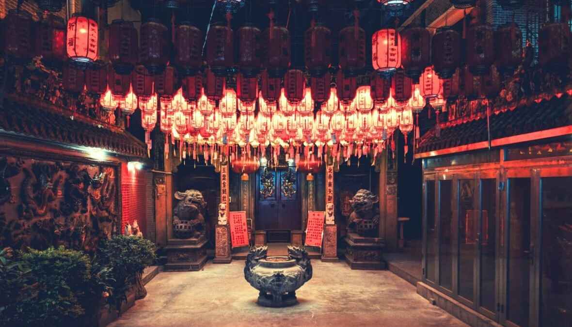 Traditioneller chinesischer Tempel mit roten Laternen und steinernen Löwenstatuen, warme Beleuchtung, geheimnisvolle Atmosphäre.