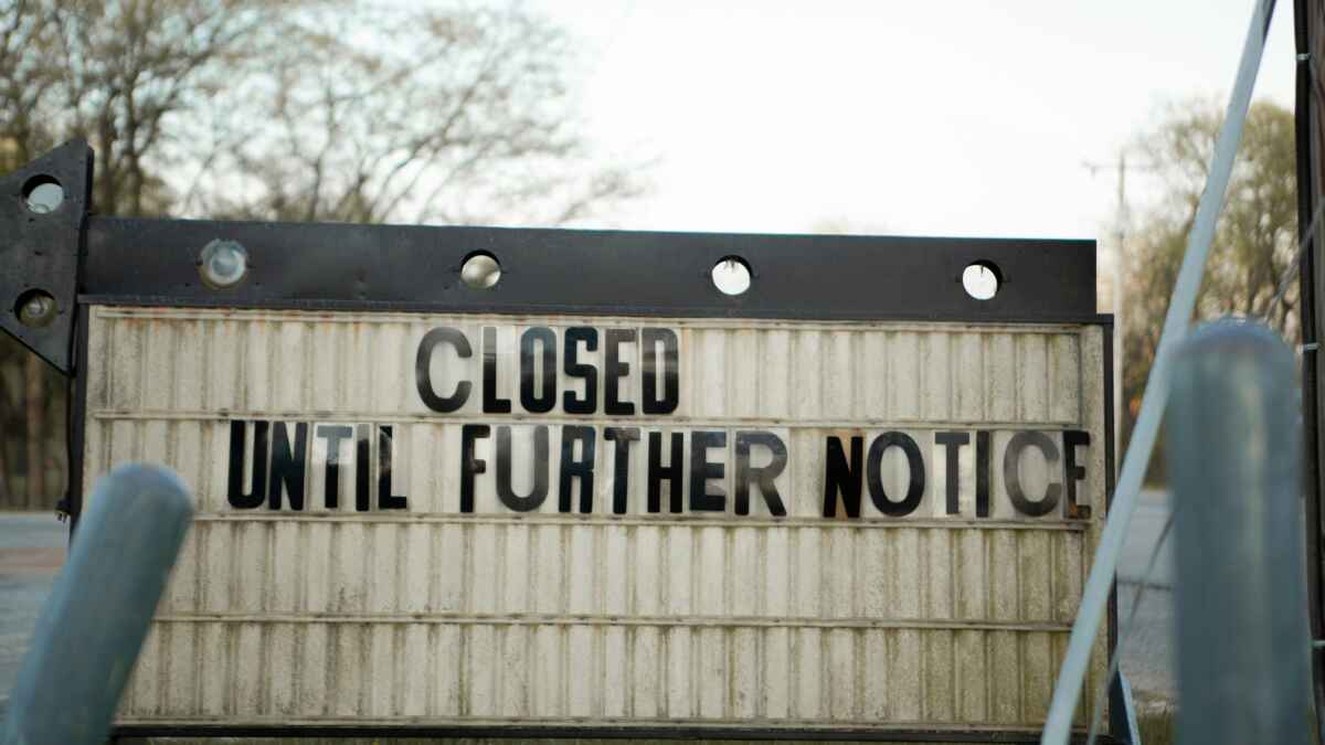 Geschlossen-Schild mit der Aufschrift Closed Until Further Notice in einer Außenumgebung, Bäume im Hintergrund.
