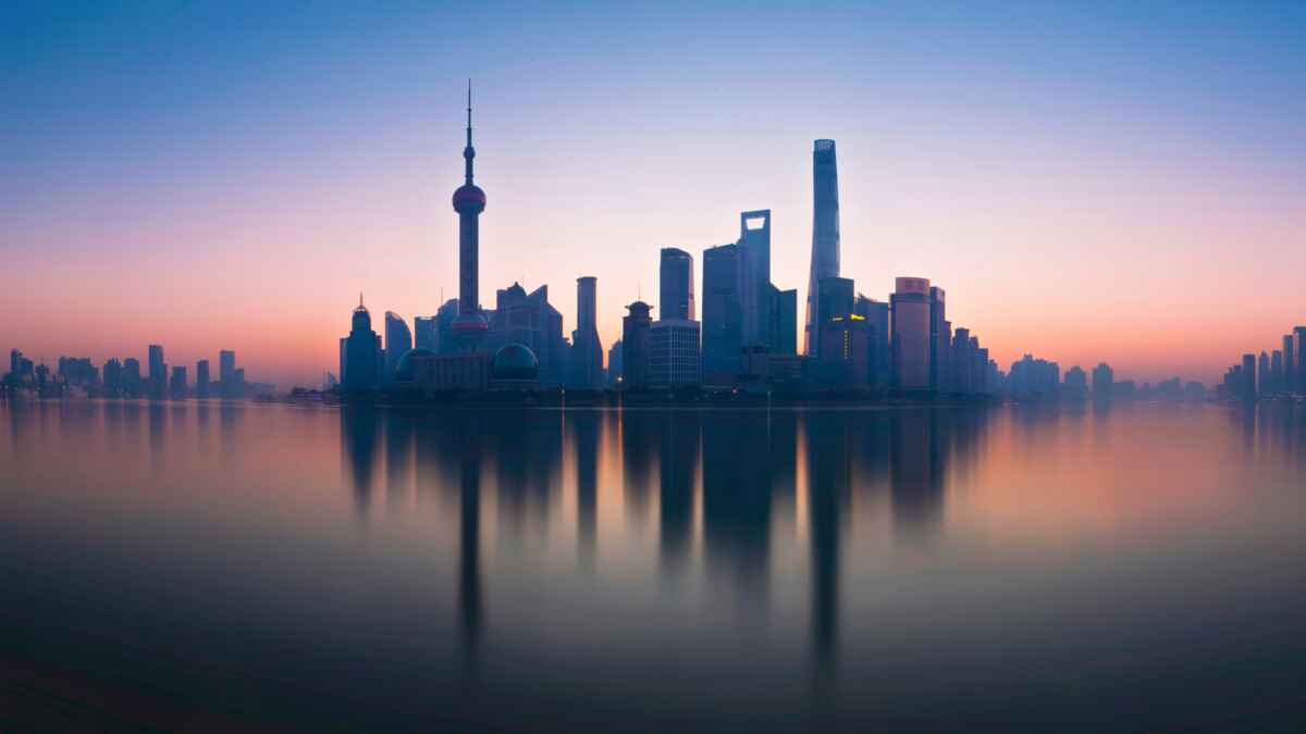 Sonnenaufgang über der Skyline von Shanghai mit dem Oriental Pearl Tower im Vordergrund, gespiegelt im Wasser.