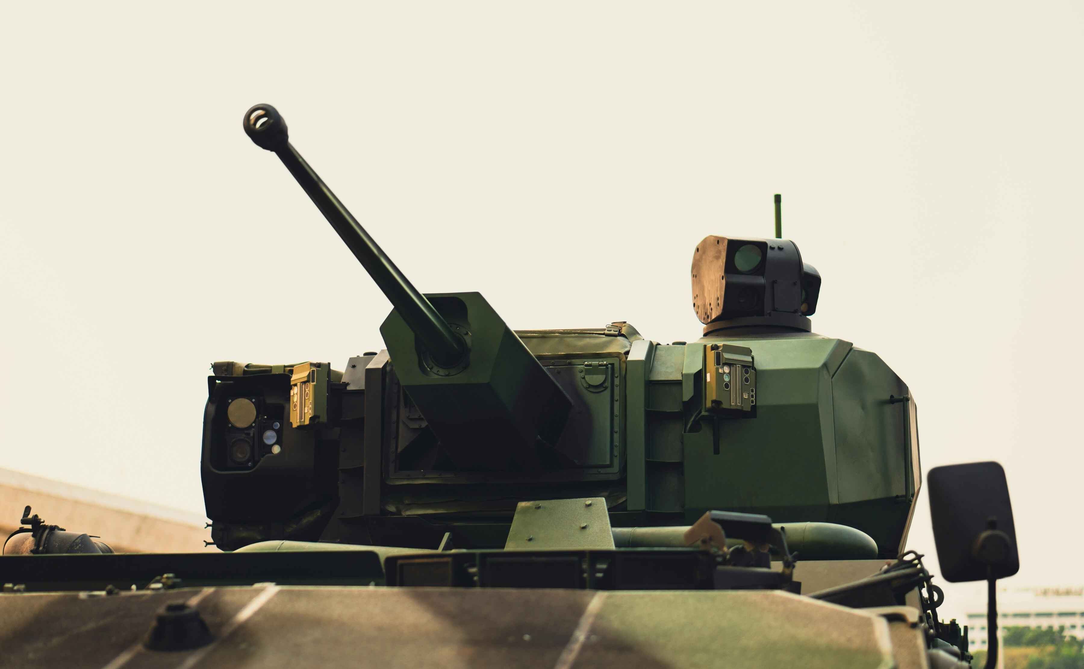 Nahaufnahme eines modernen Militärpanzers mit Geschützrohr und technischer Ausrüstung auf einem weißem Hintergrund.