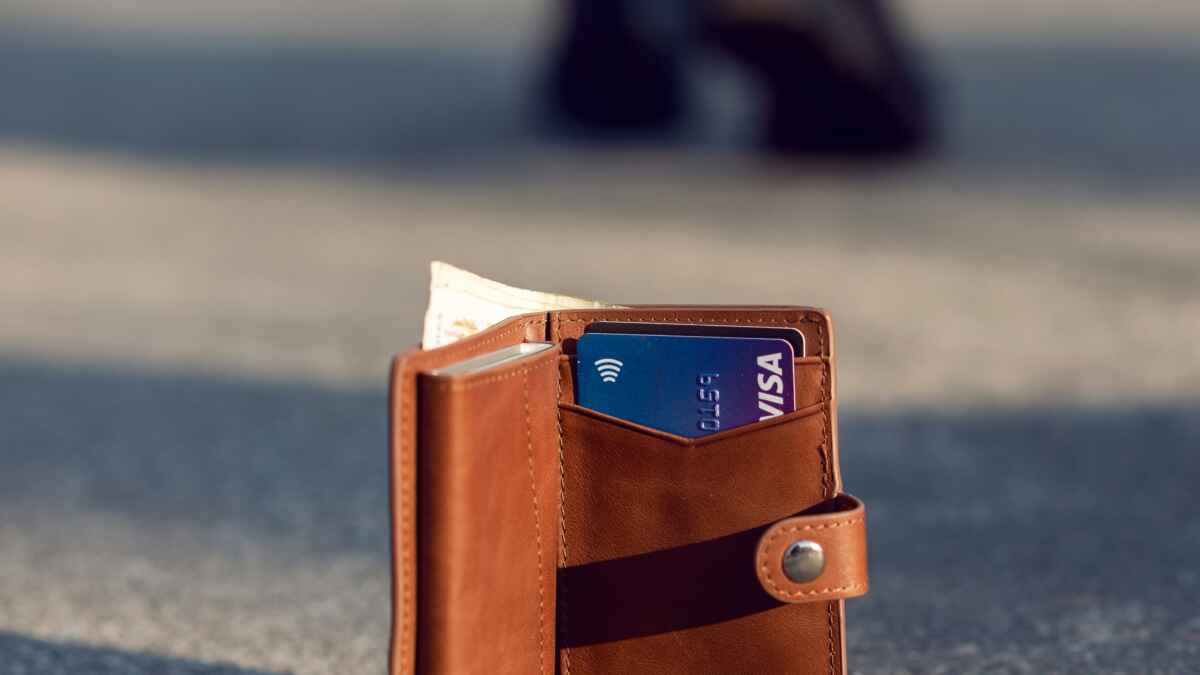 Braune Kalibrado-Geldbörse mit Kreditkarten auf einer Straße, eine unscharfe Person im Hintergrund.