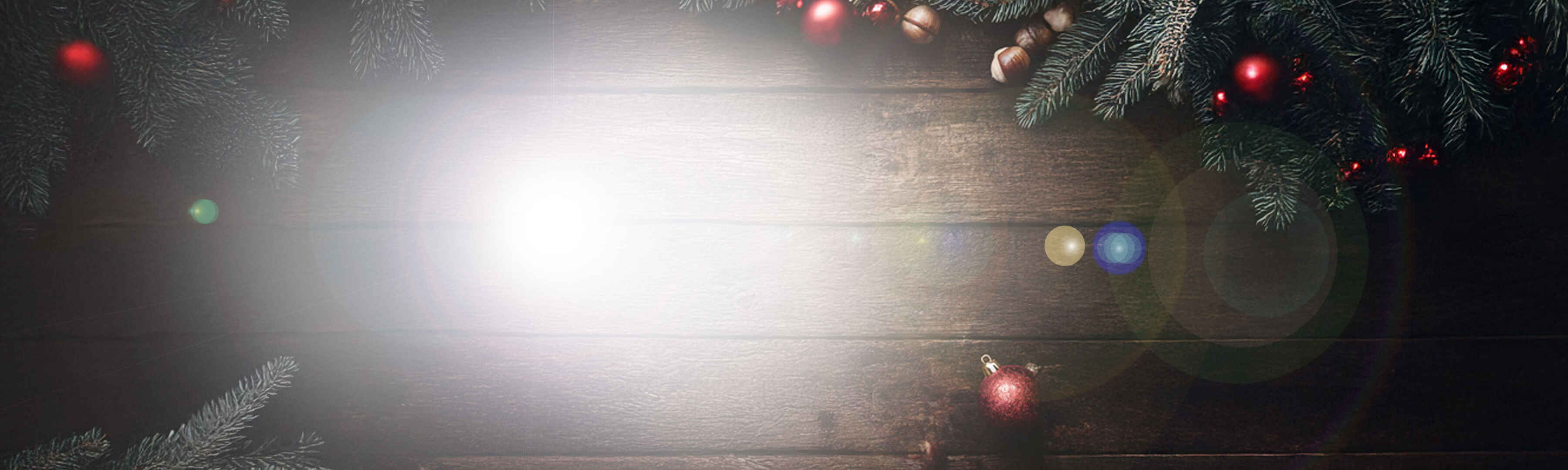 Weihnachtsdekoration mit Tannenzweigen und roten Kugeln auf Holzuntergrund, Lichtreflexion in der Mitte.