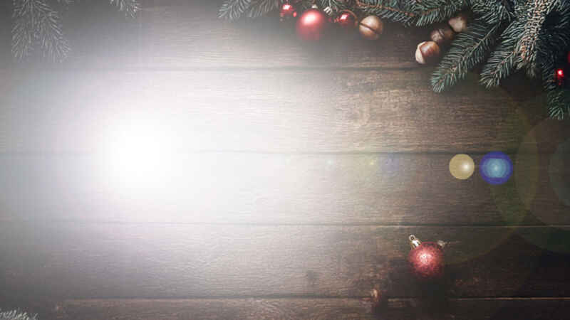 Weihnachtsdekoration mit Tannenzweigen und roten Kugeln auf Holzuntergrund, Lichtreflexion in der Mitte.