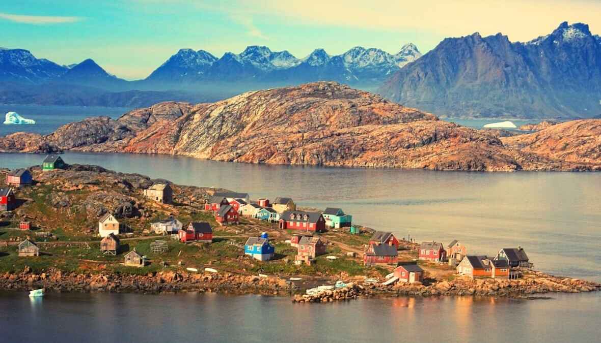 Bunte Häuser in einer malerischen Küstenstadt in Grönland, umgeben von Bergen und einem eisigen Meer.