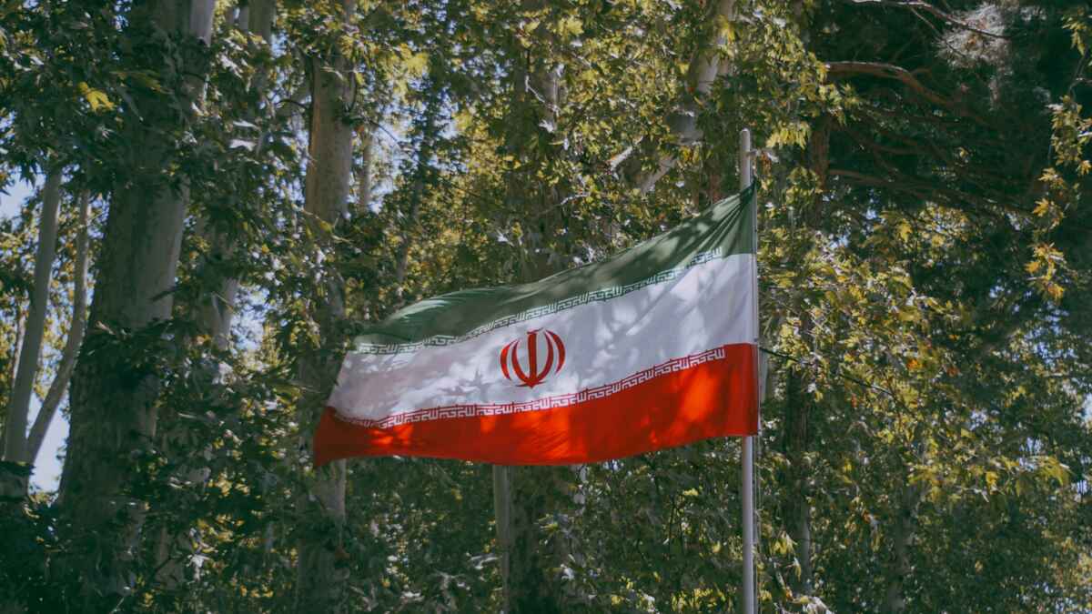 Iranische Flagge weht im Wald, umgeben von grünen Bäumen und Sonnenlicht.