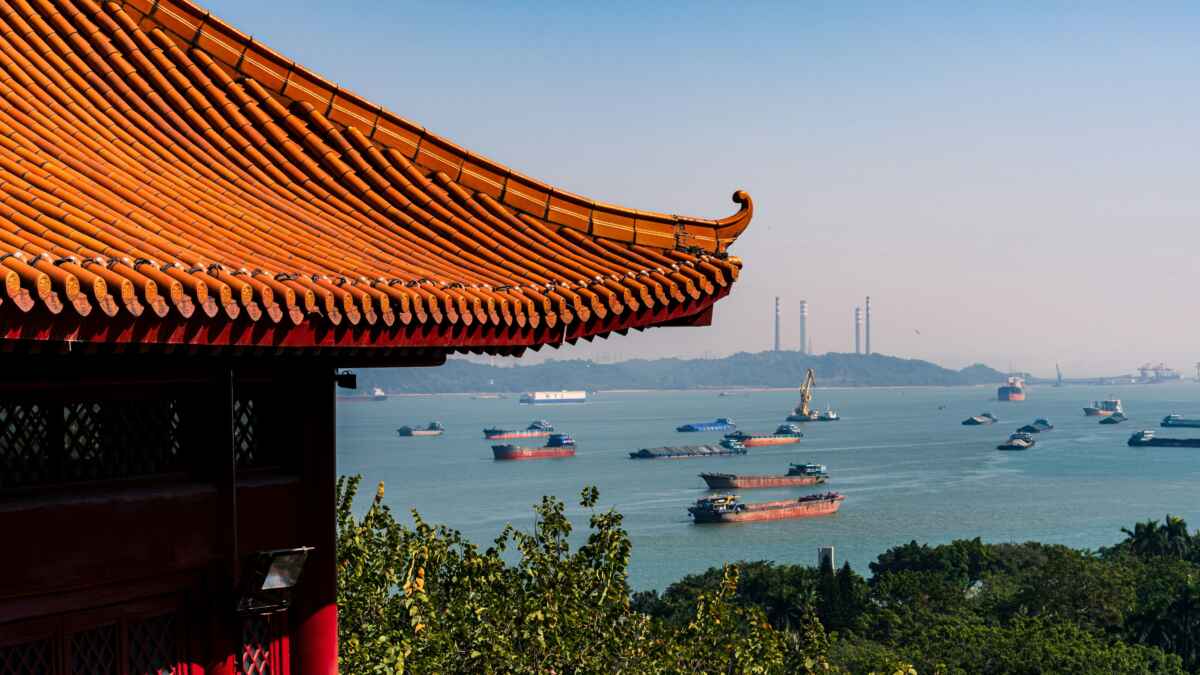 Traditionelles Gebäudedach mit Blick auf das Meer und Schiffe, kraftvolle Schornsteine im Hintergrund.