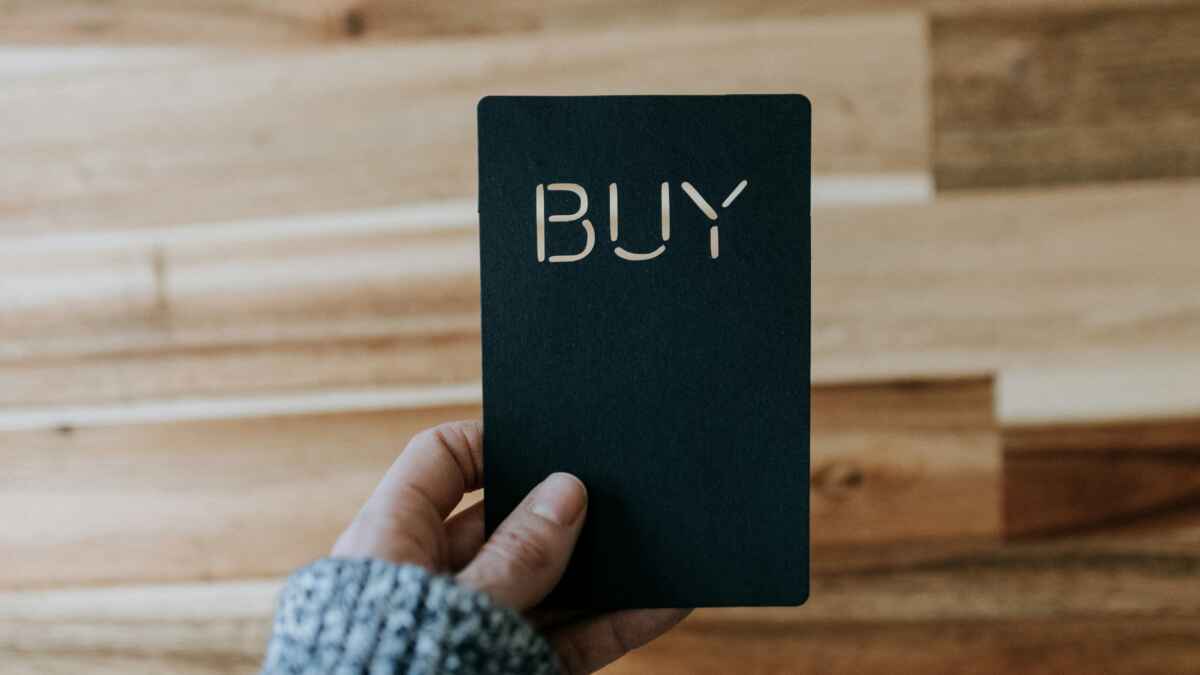 Hand hält schwarzes Schild mit dem Wort BUY auf Holzuntergrund.