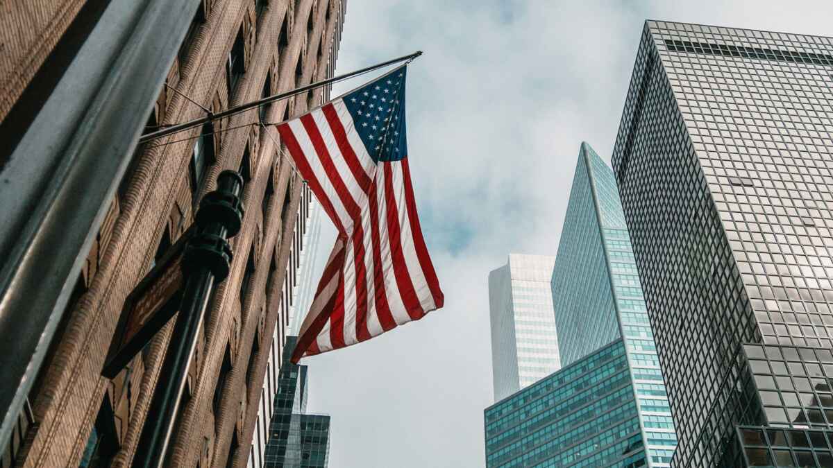 US-Flagge weht zwischen hohen Bürogebäuden in einer urbanen Skyline bei Tag.