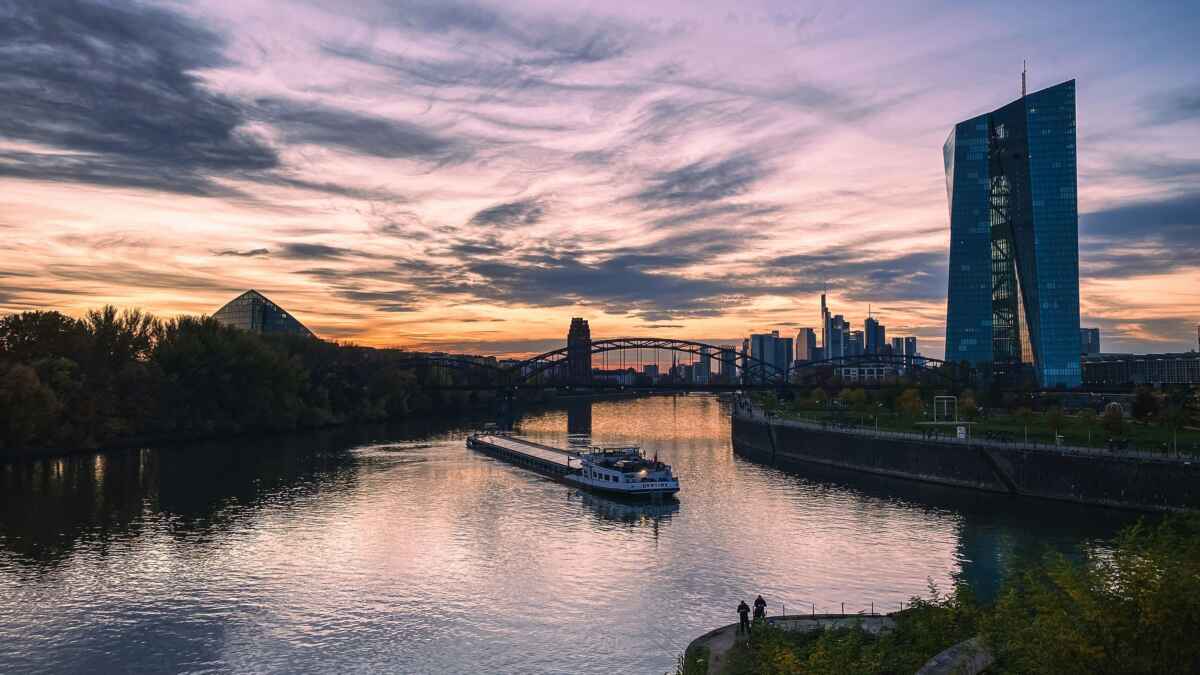 Sonnenuntergang in Frankfurt am Main: Blick auf die EZB und Skyline mit vorbeifahrendem Schiff auf dem Fluss.