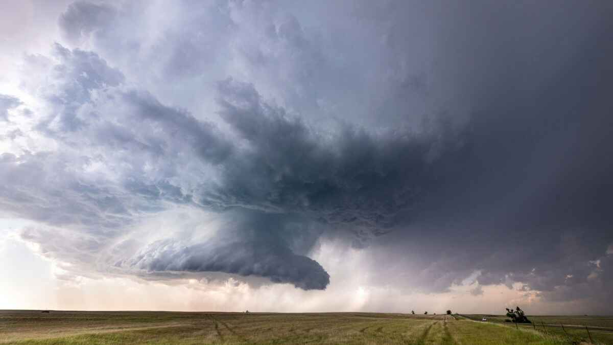 Gewaltige Superzelle über einer weiten, grünen Wiese mit dramatischen Wolkenformationen und dunklem Himmel.