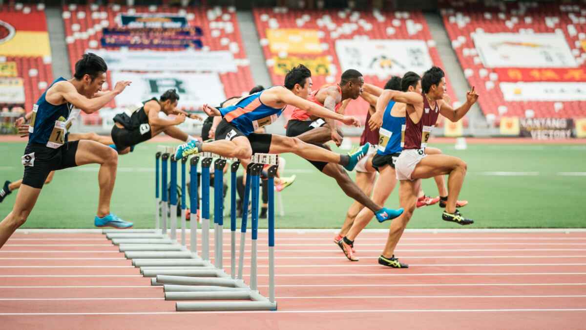 Mehrere Athleten springen über Hürden auf einer Bahn im Stadion während eines Wettkampfs.