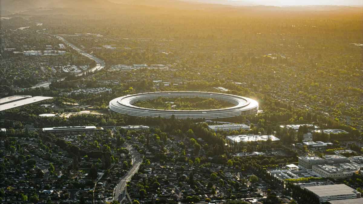 Luftaufnahme von Apple Park in Cupertino, Kalifornien, bei Sonnenuntergang, umgeben von grüner Landschaft und Stadtgebiet.