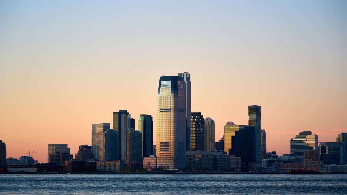 Skyline von Jersey City bei Sonnenuntergang, mit Hochhäusern und dem Hudson River im Vordergrund.