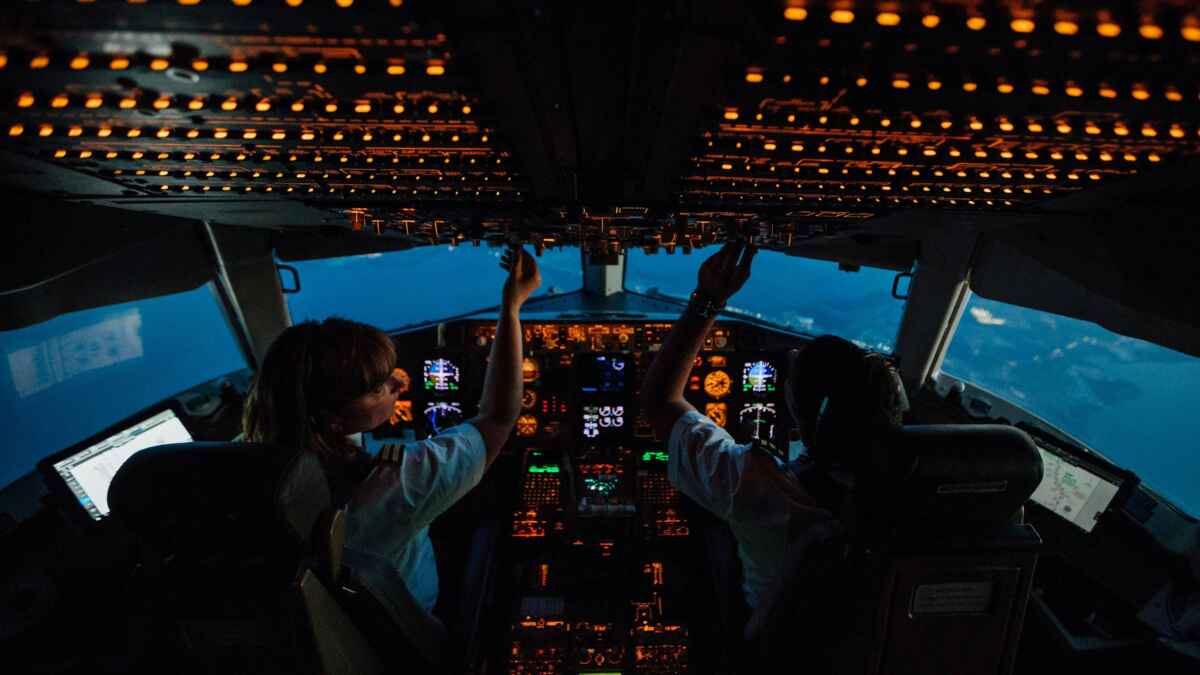 Piloten im Cockpit bei Nacht, Steuerung eines Flugzeugs mit beleuchteten Instrumenten im Hintergrund.