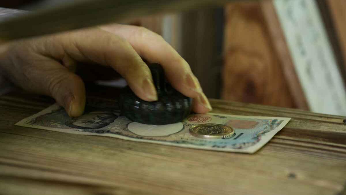 Hand stempelt Geldschein auf Holzunterlage, Münze daneben, japanische Währung.