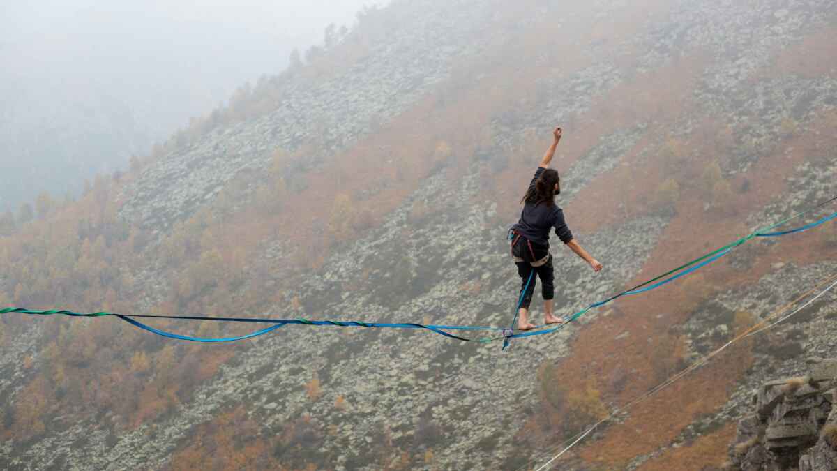 Person balanciert auf einer Slackline in nebliger Berglandschaft.