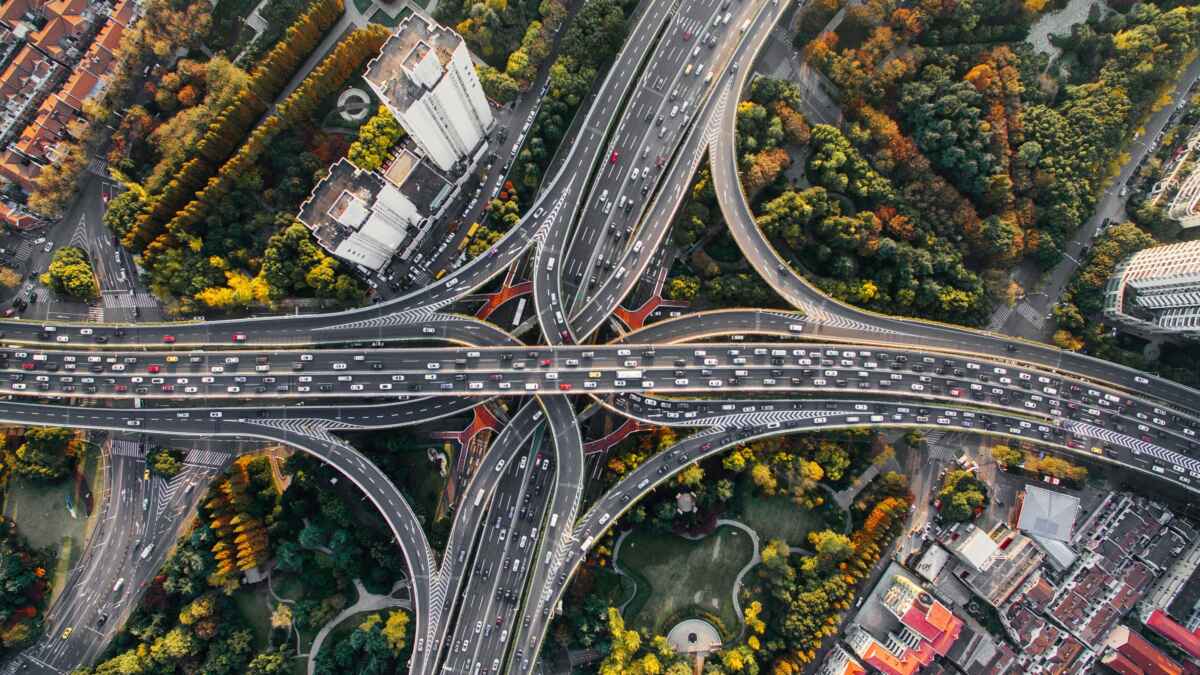 Luftbild eines komplexen Autobahnkreuzes in einer dicht bebauten städtischen Umgebung mit Parkanlagen und grünen Flächen.