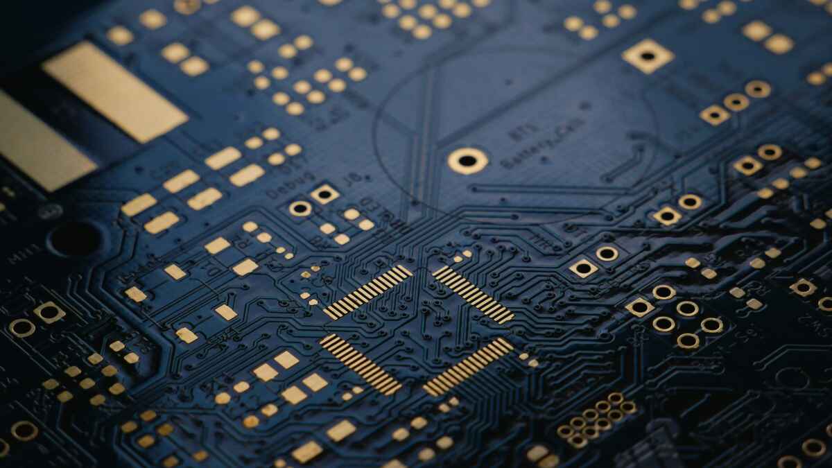 Nahaufnahme einer Computerplatine mit goldenen Leiterbahnen und elektronischen Komponenten auf dunklem Hintergrund.